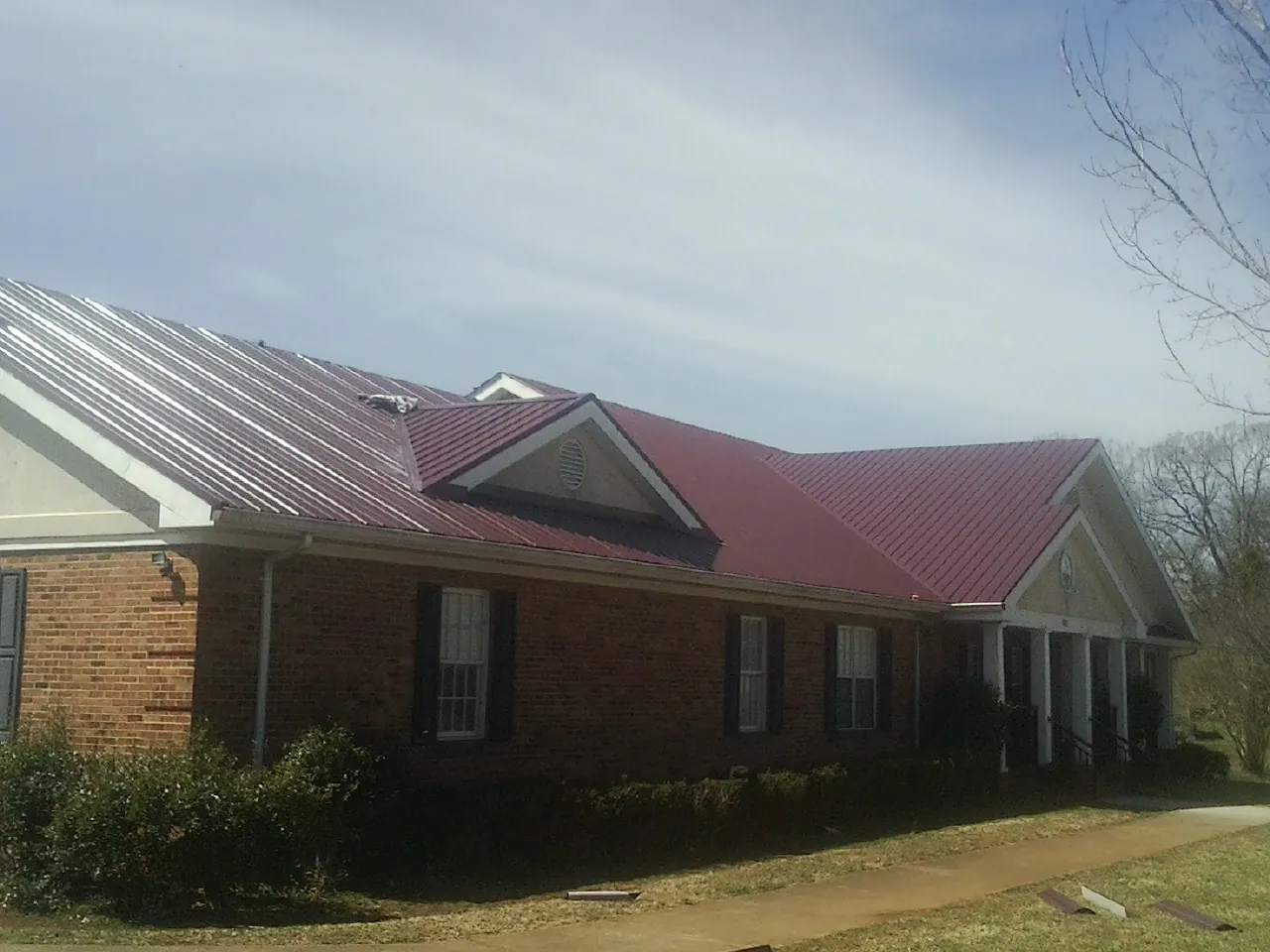 Red metal roof with gabled entries on a long brick building, from a Hail Damage Roof Repair job in Wickenburg
