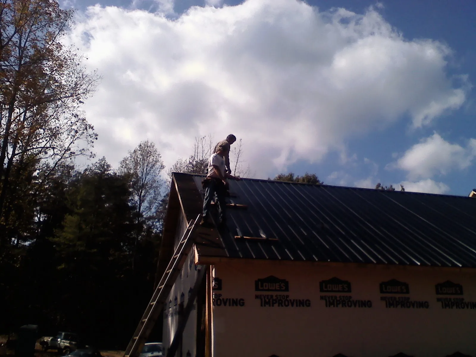 Roofer fastening dark metal panels high against a cloudy sky, from a Roof Inspection job in Wickenburg